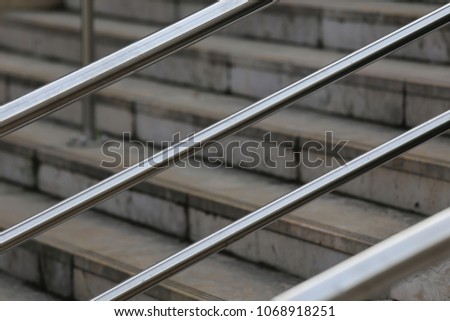 Close up outdoor view of grey urban staircases with iron handlebars. Pattern of stone steps and oblique metallic tubes. Graphic and geometric archictectural image. Modern design of a stairway.   
