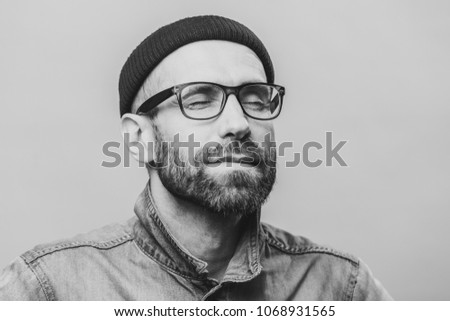 Portrait of relaxed unshaven male with closed eyes wears glasses, keeps eyes closed, enjoys calm atmosphere, isolated over white background. People, relaxation and facial expressions concept