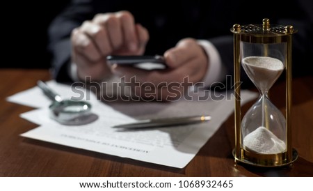 Sandglass measuring time, company director viewing electronic files on gadget