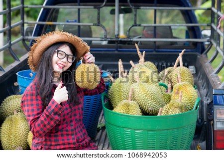 Beautyful young woman wearing red plaid shirt, hat and showing thump up sign with durian fruit in the basket on pick up car for sale,Regarded by many people in southeast asia as the king of fruits,