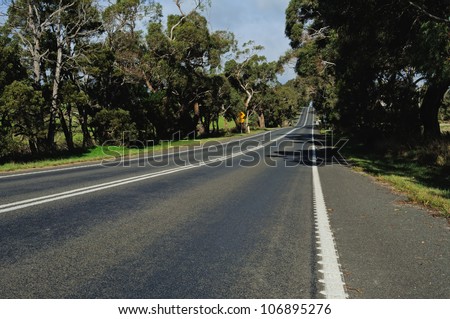 View to bended road on hills through forest from roadside edge, road sign, trees and car uphill in Victoria, Australia