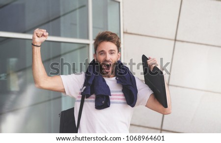 Young attractive bearded guy celebrating a winning or success with hands up. Male student style.