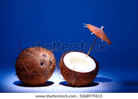 Ripe tropical coconut fruit with an umbrella isolated on a blue background