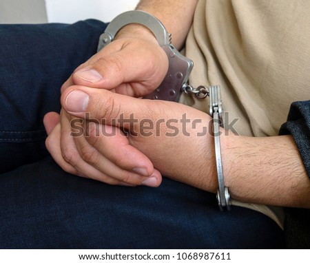 The hands of a young caucasian criminal in handcuffs, crime scene. Part of body, selective focus.