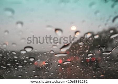 Blur image, water drops on the windshield, traffic in the city on a rainy day, car windshield view, colorful bokeh, dark background.