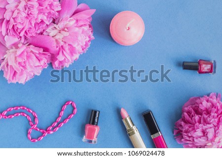 Flat lay desk with pink peonies, cosmetics and accessories on blue background