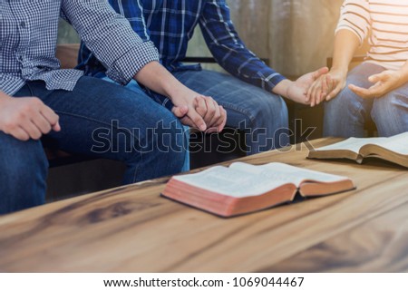 Christian group are holding hands and praying together around wooden table with holy bible