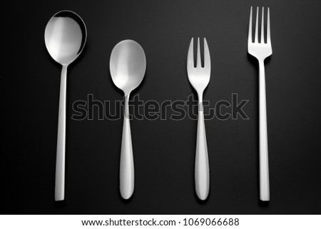 Close up a set of a silver tablespoon, teaspoon, serving fork and dessert fork on black background