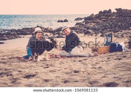 nice beautiful couple of male and female do a pic nic on the beach near thw wave with a dog border collie. love and friendship concept in summer vacation in tenerife. vintage retro colors and scenic