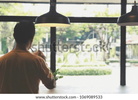 Rear view of young man looking outside coffee shop. Young man drinking ice coffee and standing alone in coffee shop. Man, Hanging lamp and ice coffee. Chill, relax, alone concept. Copy space