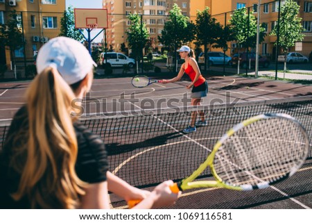 two women playing tennis outdoor. Practicing tennis on the tennis court at sunny day, on a city background
