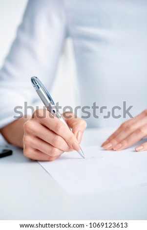 Close-up shot of businesswoman's hand holding pen and sign the paper while sitting at office desk.