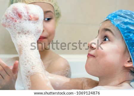 Little girls cheerfully takes a bath in the shower cap and plays with foam