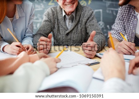 Mature teacher having talk to students by his workplace after lessons