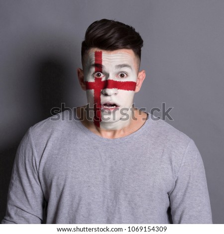 Portrait of frustrated man with the flag of England painted on his face. Football or soccer team fan, sport event, faceart and patriotism concept. Studio shot at gray background, copy space