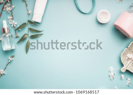 Beauty concept with facial cosmetic products, green leaves and cherry blossom on pastel blue desktop background. Modern skin care layout, top view, frame, flat lay. Branding mock up