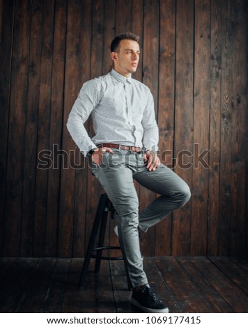 young business man in elegant modern suit sitting on a stool and looks away from the camera, Fashion. wooden background