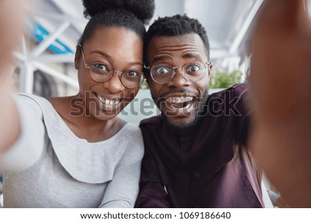 Joyful black male and female best friends have fun together, take picture of themselves or pose for making selfie, being in good mood after successful day. People, friedship, leisure, happiness