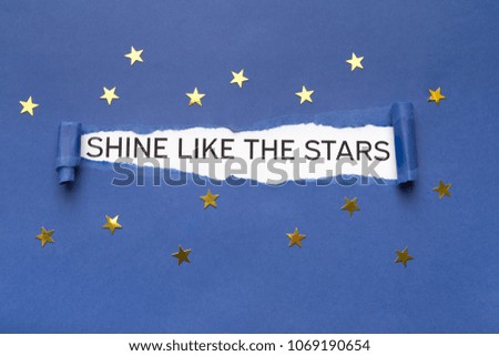 Inspirational phrase Shine like the stars appearing behind torn blue paper with small golden stars.