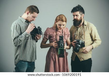 Men in checkered clothes, retro style. Company of busy photographers with old cameras, filming, working. Men and woman on pensive faces on grey background. Vintage photography concept.