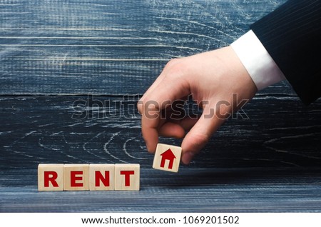 The hand holds a cube with a house symbol for the word lease. Rent and rent of a house for rent, apartment and real estate search. Own house or rental housing
