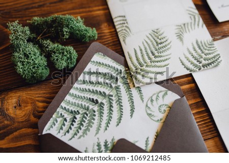 White invitation letter for wedding decorated with fern and brown envelope lie on the table