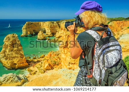 Travel photographer takes shot of iconic natural arches of Praia da Marinha in Algarve. Female tourist takes pictures with professional camera of high cliffs of popular Marinha Beach. Trip in Portugal