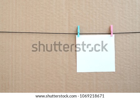 White blank card on rope on a brown cardboard background. Creative reminder, small sheet of paper on wooden clothespin, memo backdrop