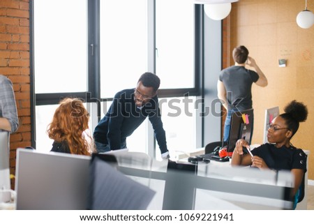 nice african office assistants are greeting Caucasian woman with long red hair while man on the background of the picture is having serious conversation