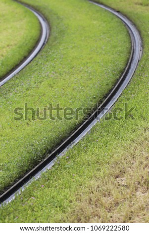 Close up outdoor view of tramway curved rails with green grass. Unban picture of parallel rails in large lawns. Abstract image of transportation by train and tram. Geometric shapes on the ground.
