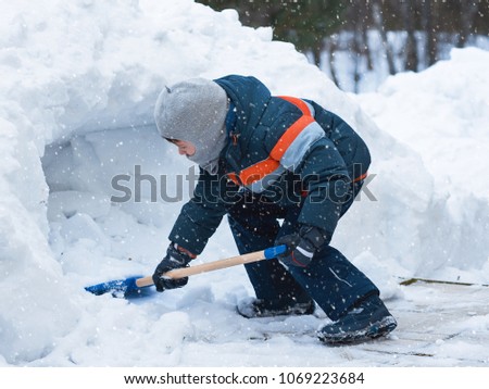 European boy is playing in the yard. He is making snow cave.