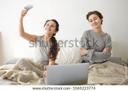 Picture of teenage girl and her mother or elderly sister sitting on bed in front of open laptop, shopping online, ordering food delivery or buying new clothes, browsing web stores using credit card