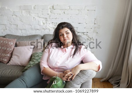 Picture of sad beautiful young Caucasian woman in casual clothes having upset look after she failed to keep healthy sugar free diet, dreaming about slim perfect body in modern living room interior