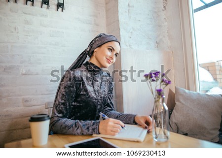 beautiful muslim woman writing on paper at cafe