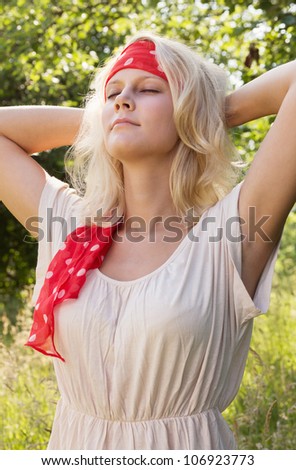 Daydreaming young blond woman with closed eyes and headband. Summer outdoor portrait against a blurry green background.