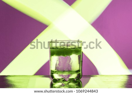 Liquid with ice in a glass on a reflective surface on a reddish background