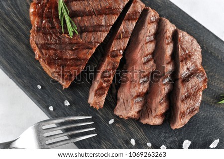 Juicy beef steak cooked on the grill. The steak is cut into slices and lies on a dark wooden board. In the picture there is a fork. View from above. Close-up. Macro photography.