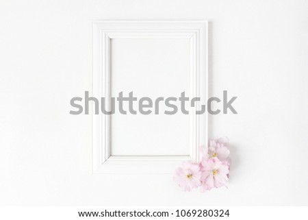 White blank wooden frame mockup with pink Japanese cherry blossoms lying on the white table. Poster product design. Styled stock feminine photography. Home decor. Spring concept.