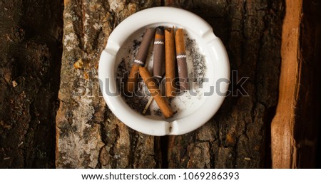 Cigarette with ashtray on wood table, cigarette butts vintage background. White ashtray on wooden bricks