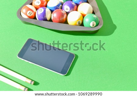 Mobile phone and billiard balls on a green color pool table background. Close up top side view mockup smartphone screen copyspace. Entertainment communication technology recreational design