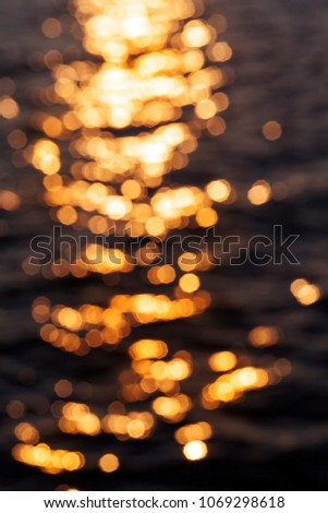 black surface of water with waves from the wind, time of day at dusk, close-up, the surface is defocused and on the water there is a strip with glare from the setting sun