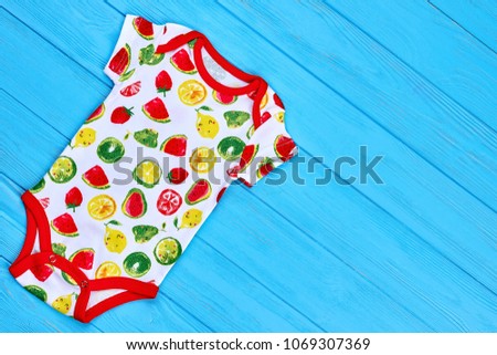 Fruit print bodysuit, top view. Natural cotton baby-girl summer romper and copy space, blue wooden background. Newborn cotton wear.