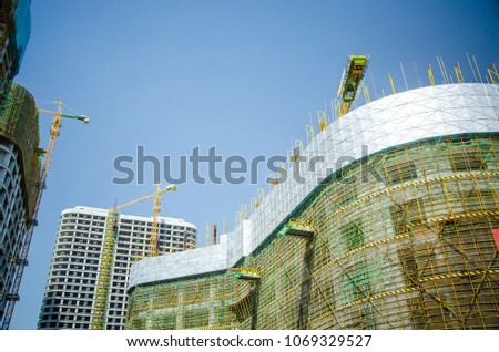The construction of high-rise buildings.Crane,scaffolding and building against blue sky.Safety Health and Environmental to construction site background.