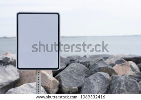 Empty sign with blurred background with boulders, and water.
