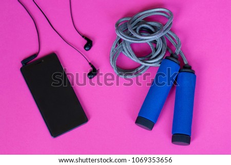Jump rope and smartphone with headphones on pink background.  Top view.