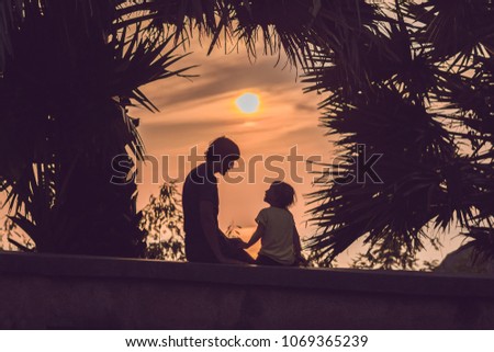 Silhouettes of the father and son, who meet the sunset in the tropics against the backdrop of palm trees