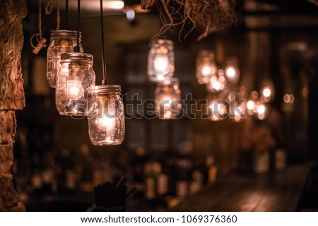 DIY light lamps hanging lamps made from glass jars at counter bar with blurry wine shelf background Royalty-Free Stock Photo #1069376360
