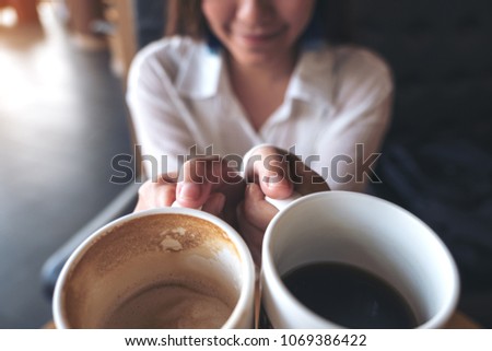 Close up image of a woman holding two white coffee mugs in cafe