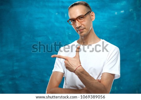 Portrait of young cute positive man showing by finger something useful on blue background. Place for text