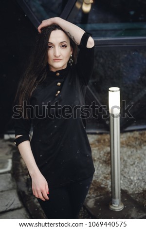 Street Portrait of a woman. fashionable brunette in black clothes on style, a walker  open air in seasons. snowfall snowflakes in frame